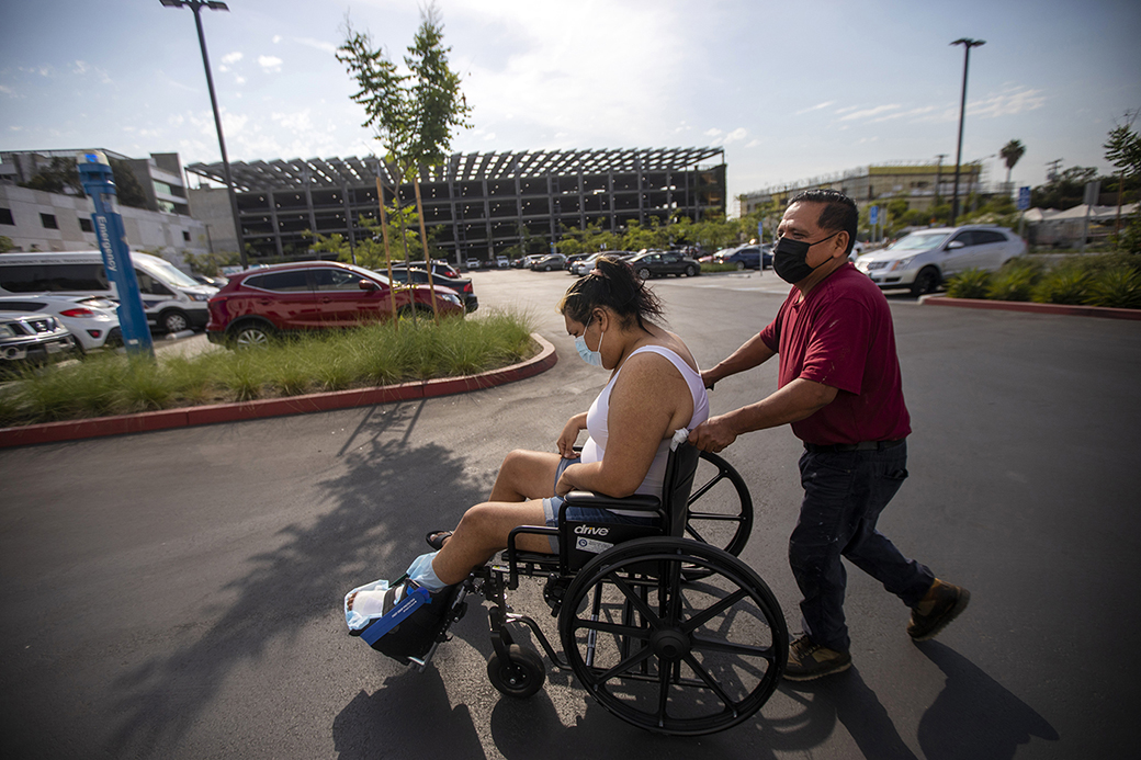 A man guides his stepdaughter in a wheelchair through a parking lot outside a wound care clinic in Los Angeles, 2021. His stepdaughter is transgender. (Getty/Francine Orr/Los Angeles Times)