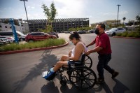 A man guides his stepdaughter in a wheelchair through a parking lot outside a wound care clinic in Los Angeles, 2021. His stepdaughter is transgender. (Getty/Francine Orr/Los Angeles Times)