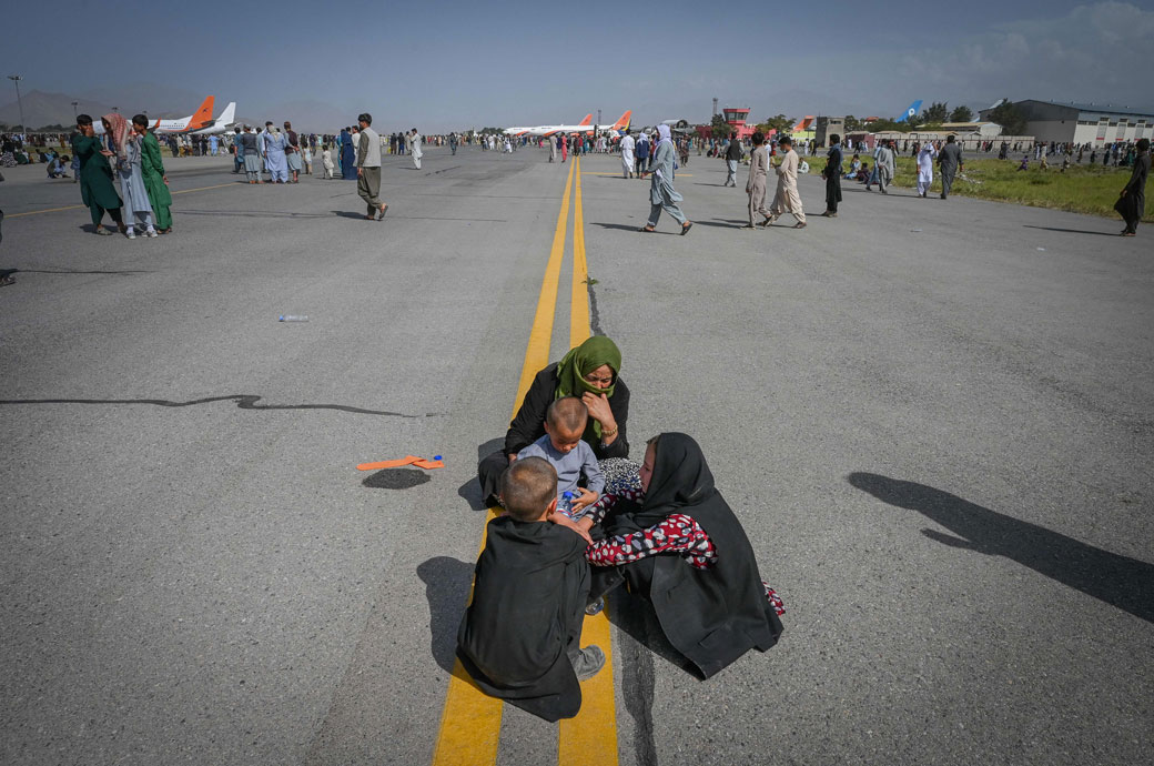 Afghan people sit along the tarmac as they wait to leave the Kabul airport in Kabul, August 2021. (Getty/Wakil Kohsar)
