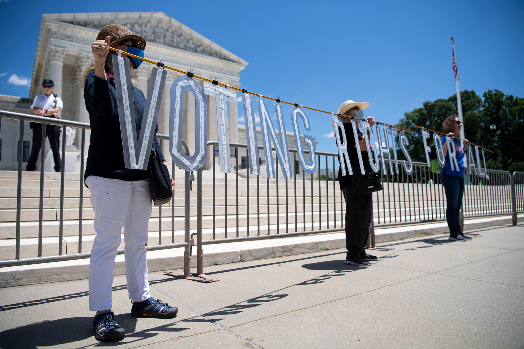 Three demonstrators hold a sign advocating for voting rights for all outside of the U.S. Supreme Court building.