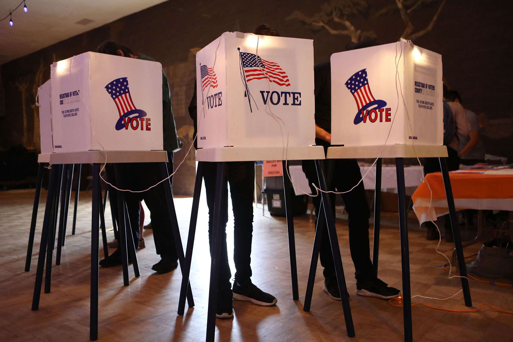 A group of voters is seen filling out their ballots in voting booths at a polling place.