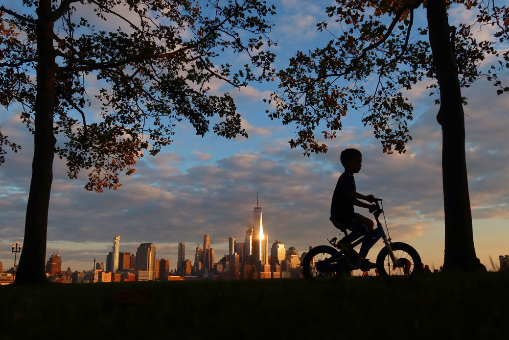 A child rides his bicycle through a park in Hoboken, New Jersey, as the sun sets on lower Manhattan and One World Trade Center in New York City on October 5, 2020. (Getty/Gary Hershorn)