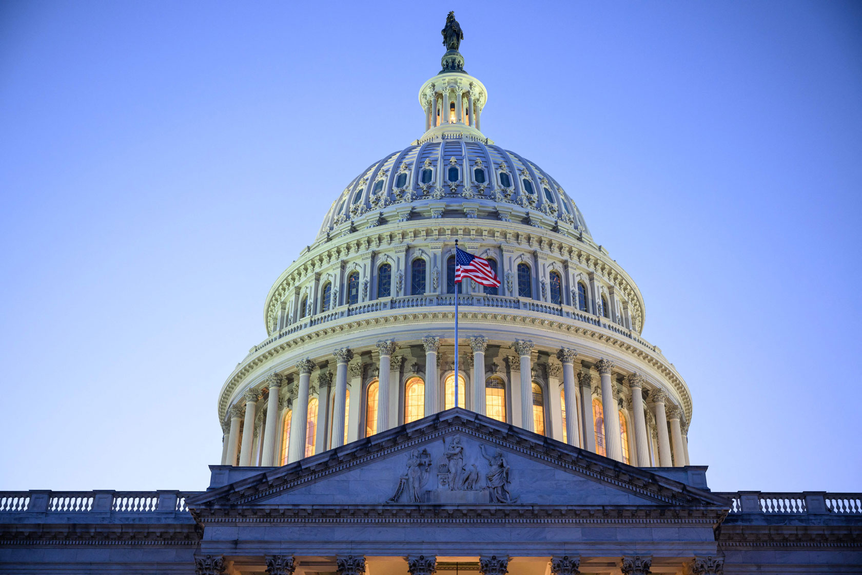 The U.S. Capitol building is seen at dusk with a clear blue sky in the background.