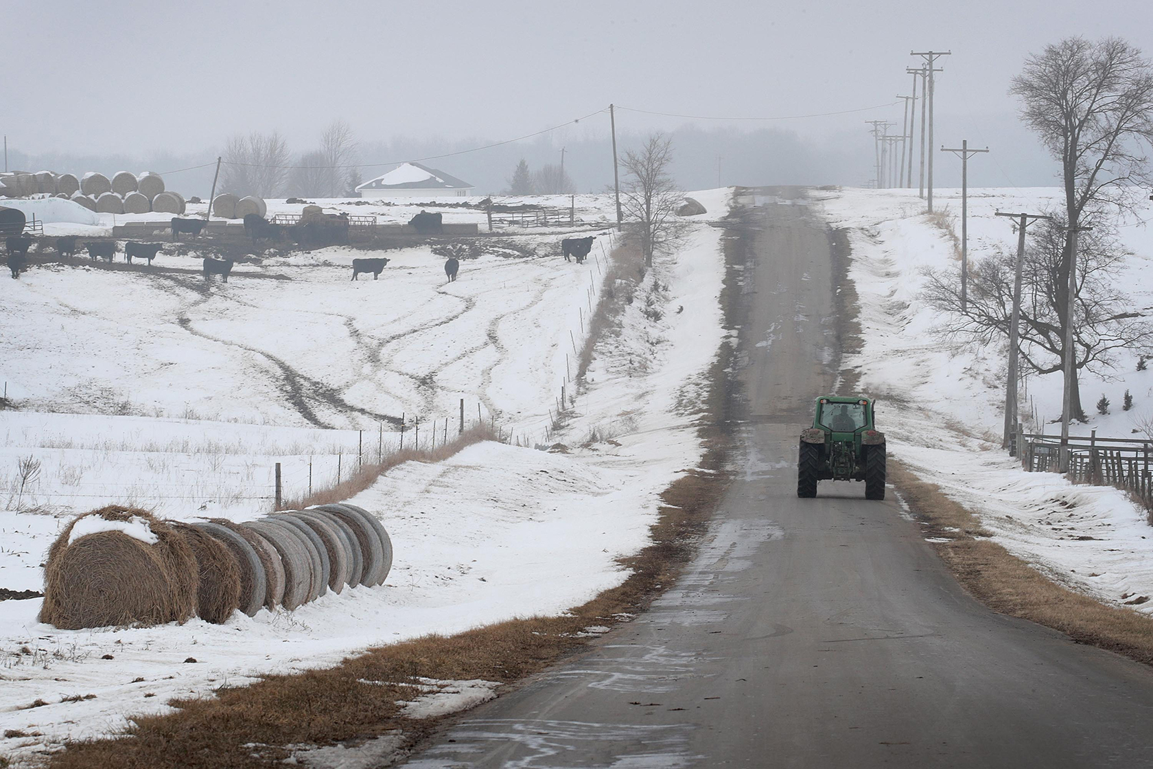 A tractor drives down a rural road in winter.