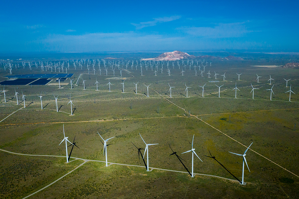 View of landscape from above showing several windmills against a bright blue sky and grass fields.