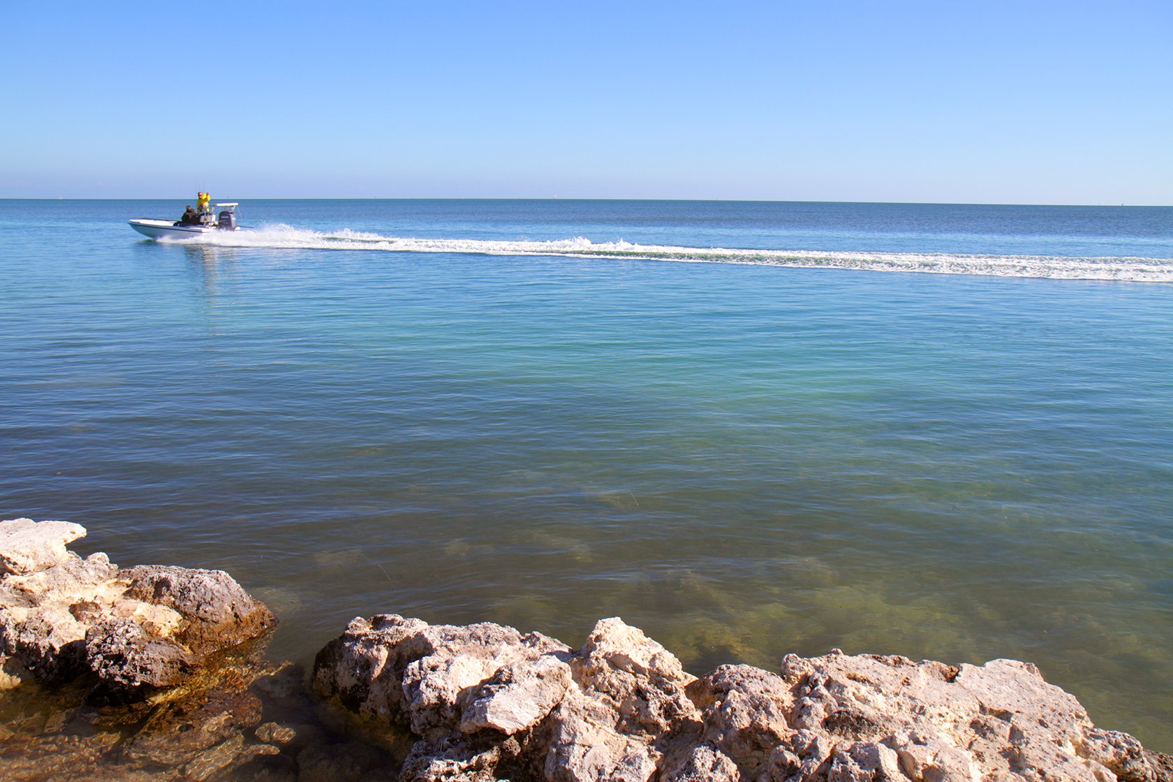 View of the ocean during the day from a rocky shoreline. A small motor boat is seen in the upper left.