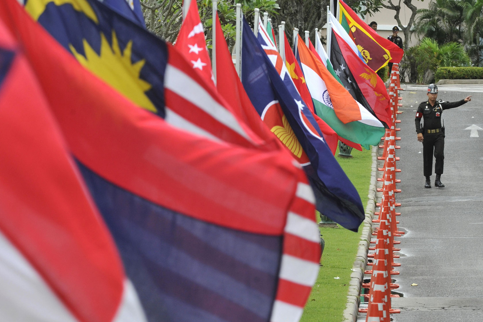 A soldier gestures from his position securing a road lined with the flags of member countries of the Association of Southeast Asian Nations (ASEAN), as well as regional dialogue partner countries.
