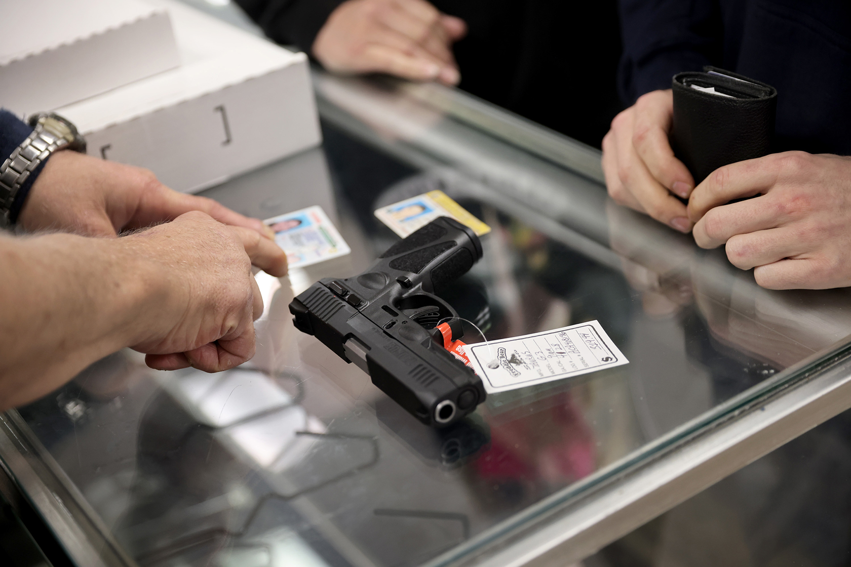 Customer purchases a black gun, passing his ID/driver's license over the glass counter.