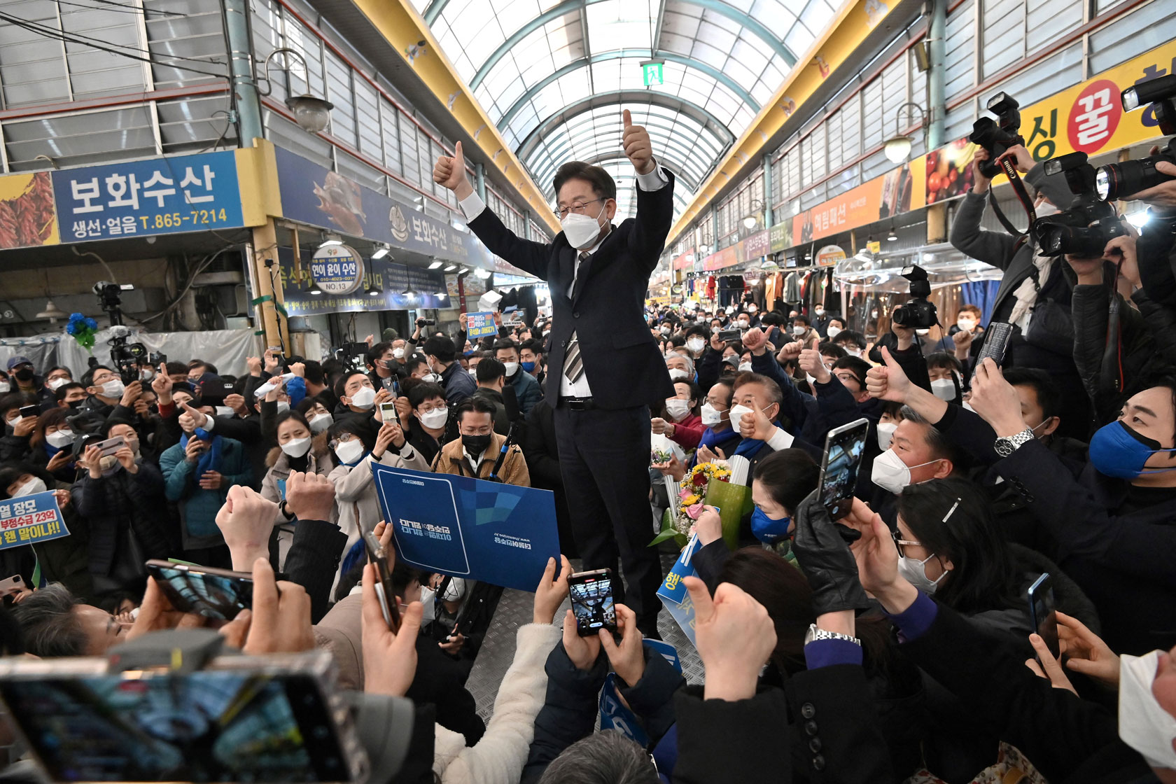 This picture taken on February 12, 2022 shows South Korean presidential candidate Lee Jae-myung (C) of the ruling Democratic Party waving to supporters during an election campaign at a market in Sejong ahead of the March 9 presidential election. - Lee, a school dropout maimed in an industrial accident as a teen, is the ruling Democratic Party's maverick candidate in the March 9 election.