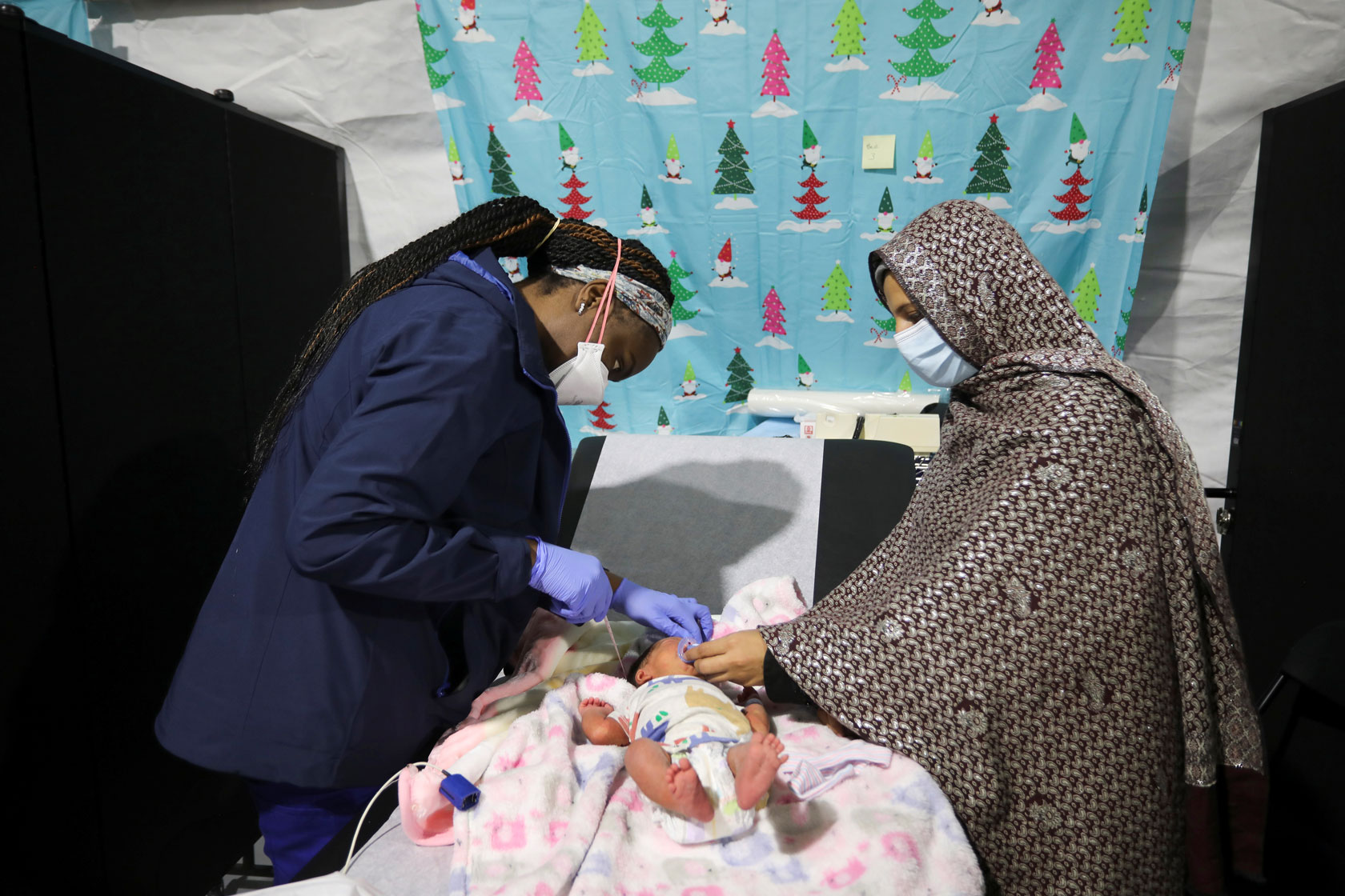 A nurse, right, attends to a 9-day-old child as the child’s mother looks on.