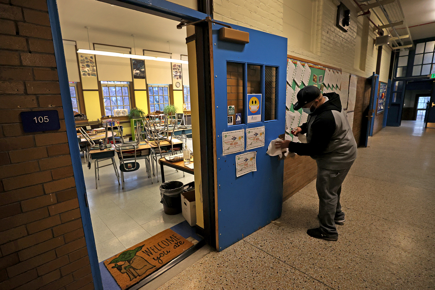 A custodian standing in hallway cleaning classroom doorknob