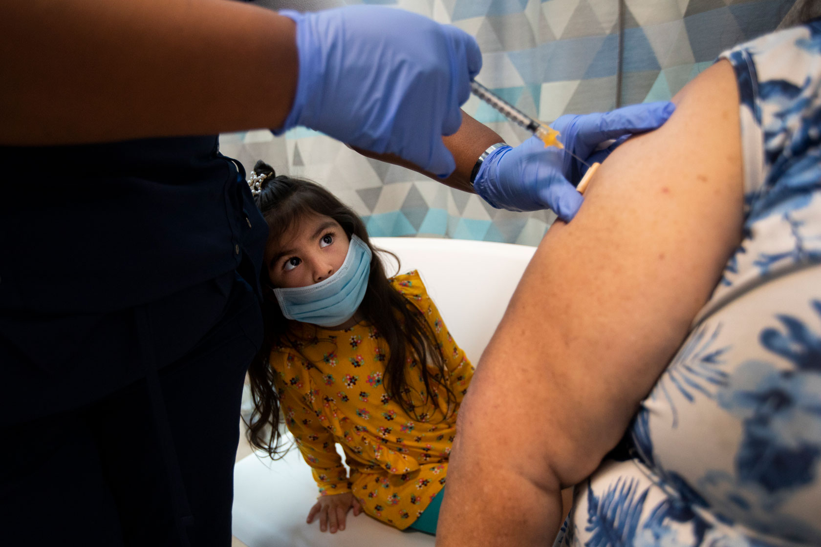 A 3-year-old girl keeps a close eye on the needle as both her grandparents are vaccinated.