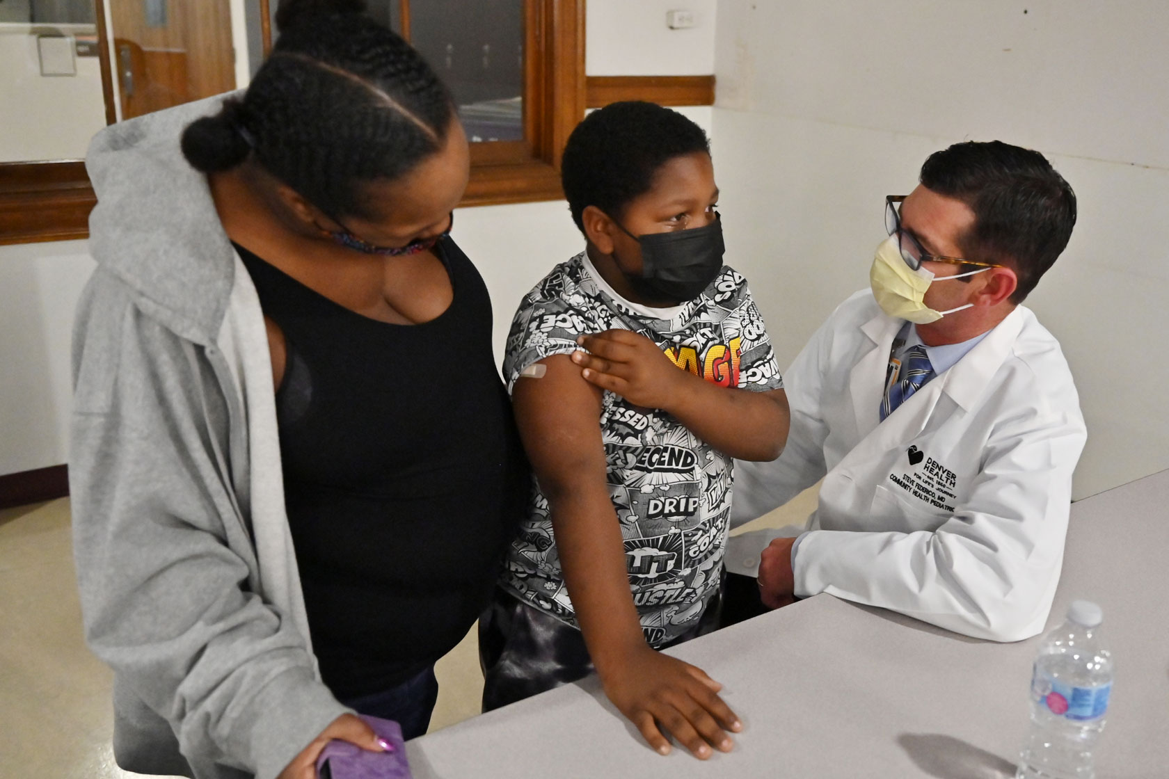 A doctor, right, comforts an 8-year-old boy after his first vaccine shot as his mother looks on at a clinic in Denver.