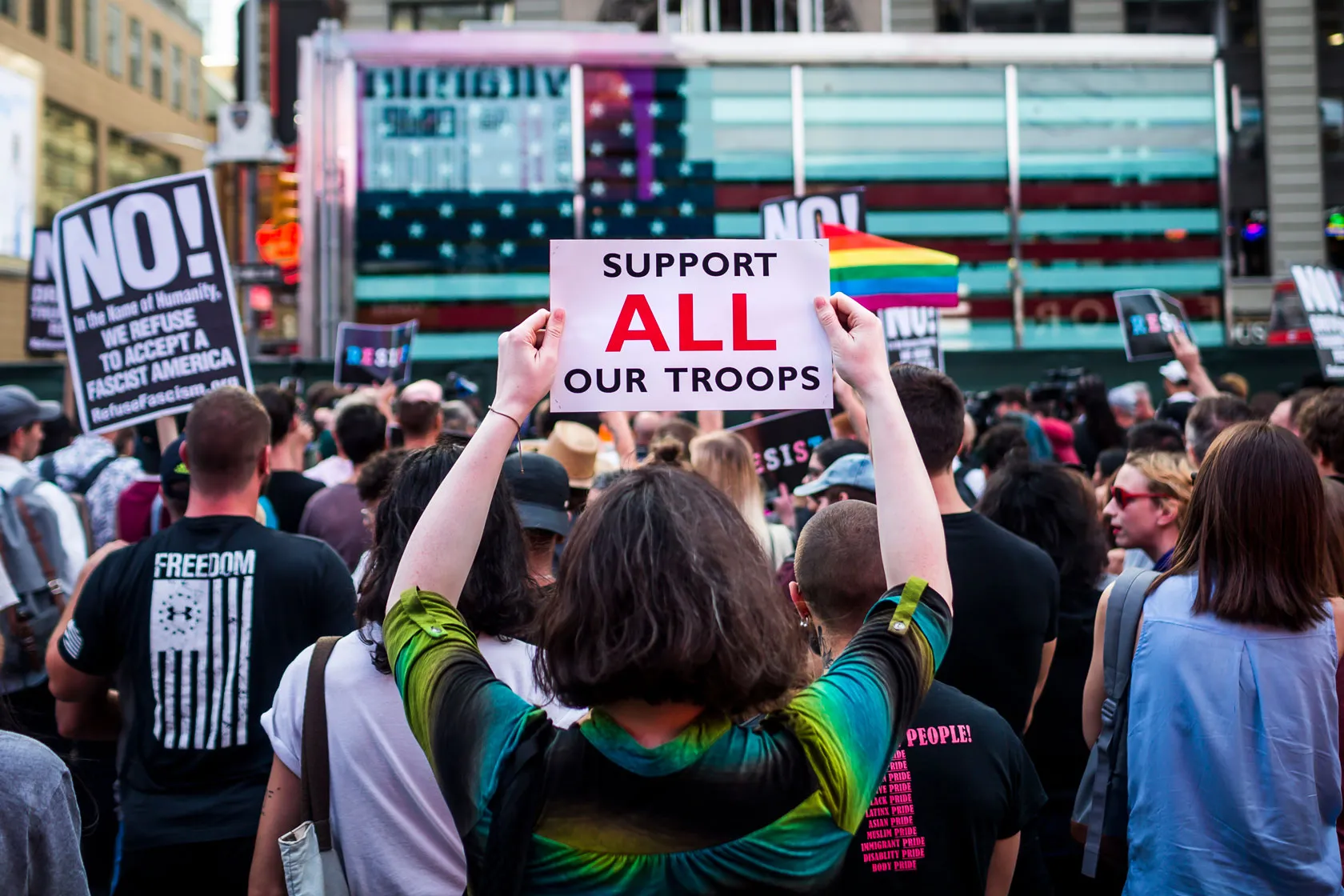 Thousands of people take the streets to protest then-President Donald Trump’s proposal to ban transgender people from serving in the military. The person in the foreground holds a sign that says 