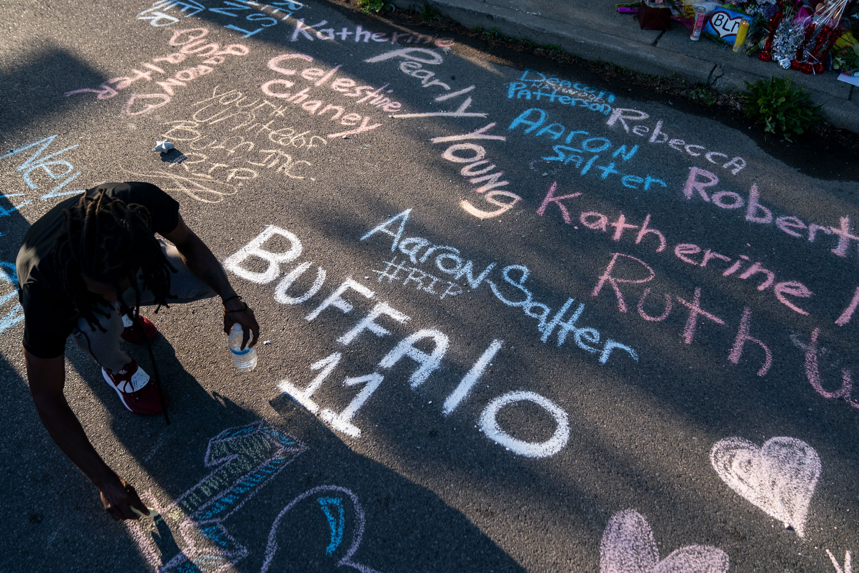 A resident adds to a sidewalk chalk mural depicting the names of those killed during the Buffalo mass shooting.