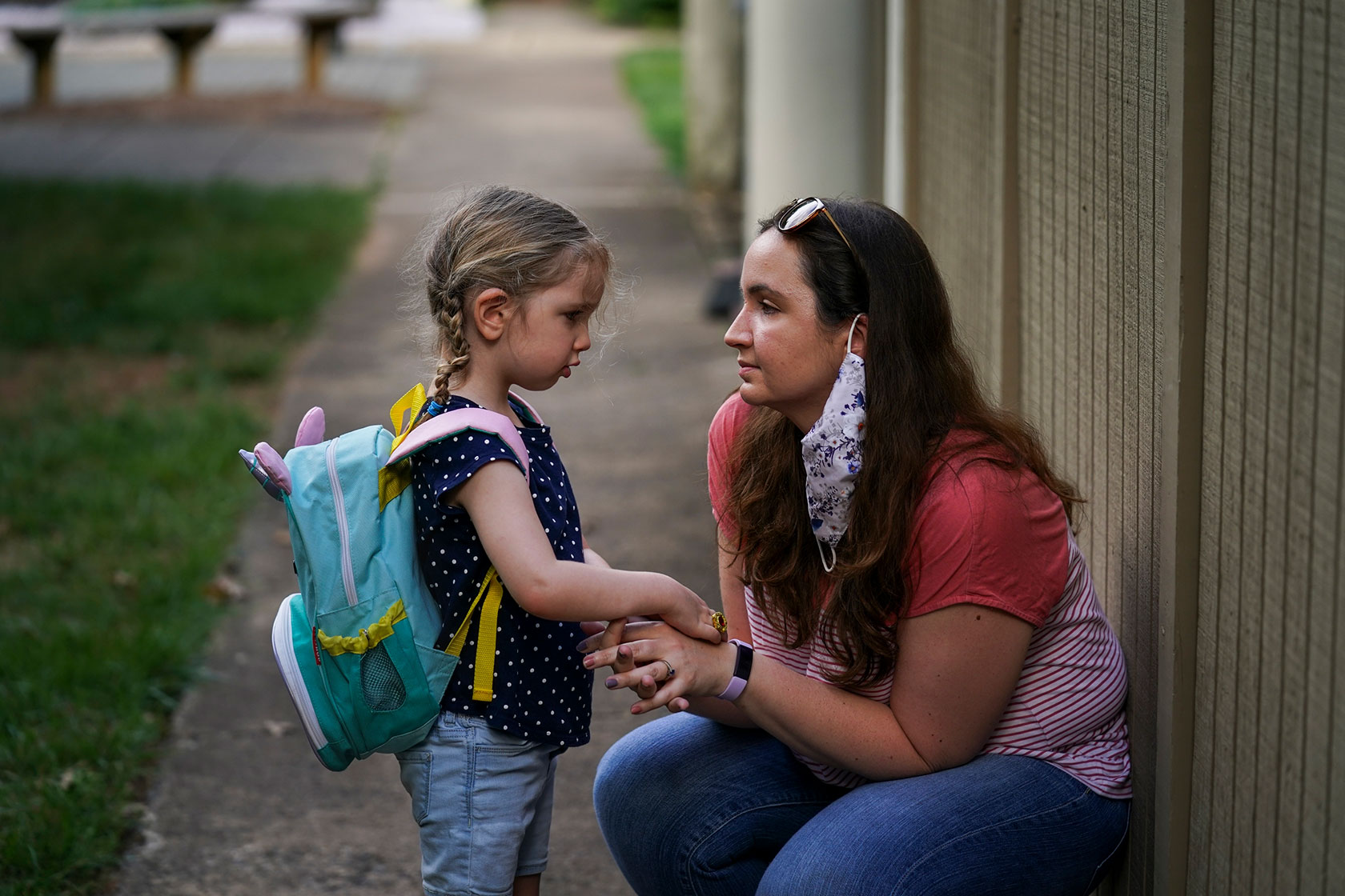 Photo shows a woman kneeling and holding her young daughter's hands.