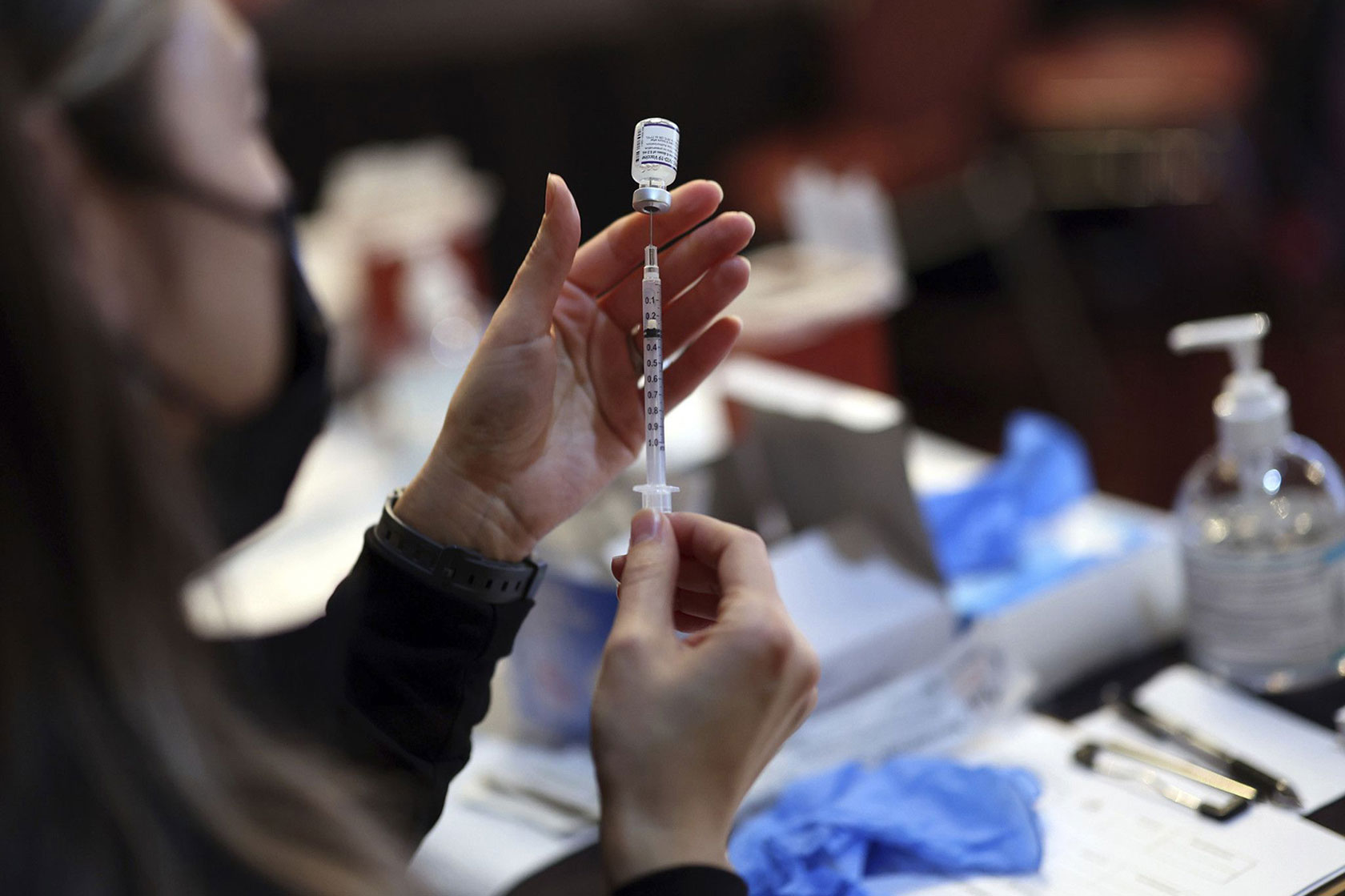 Photo shows a nurse using a syringe to withdraw a dose of the Pfizer vaccine from a vial.