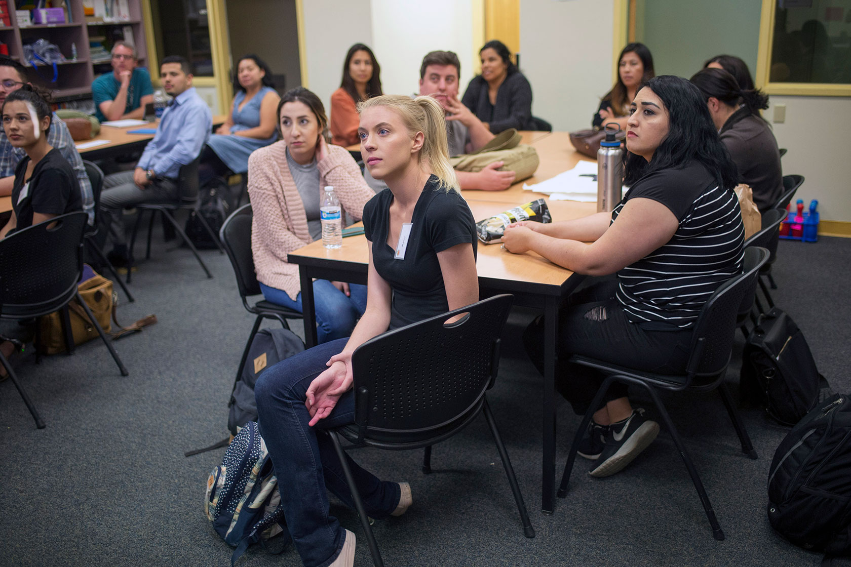 Photo shows a group of adults seated around tables in a classroom.