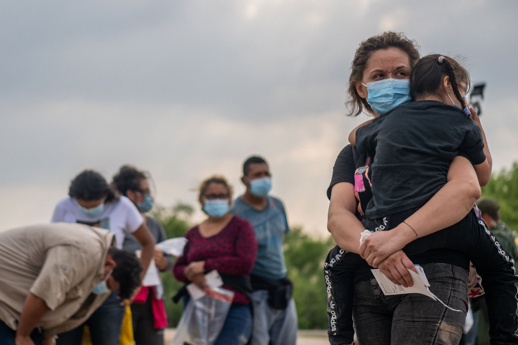 Photo shows a mother carrying her young daughter, surrounded by other individuals wearing face masks.