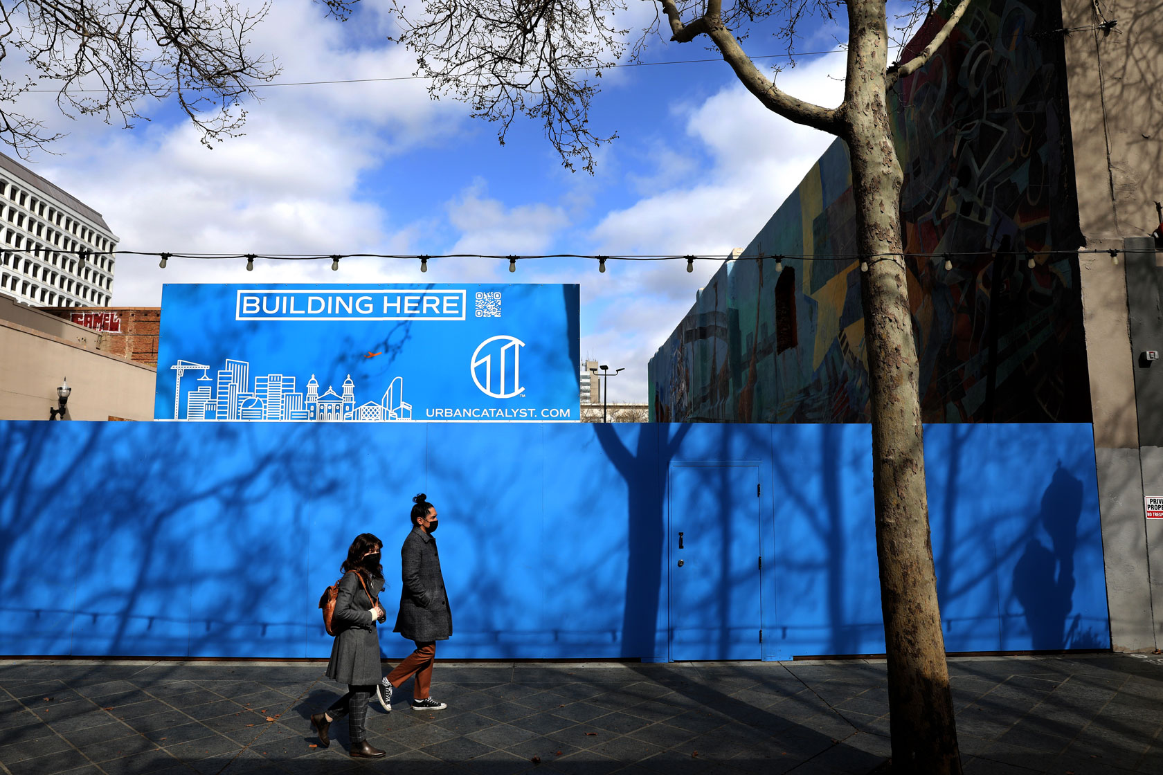 Two people walk past a future site for a new building in San Jose, California.