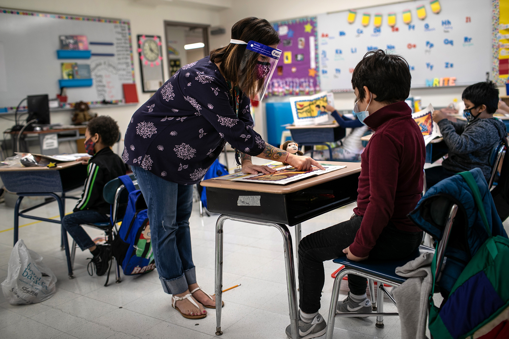 Teacher standing while helping student seated at desk