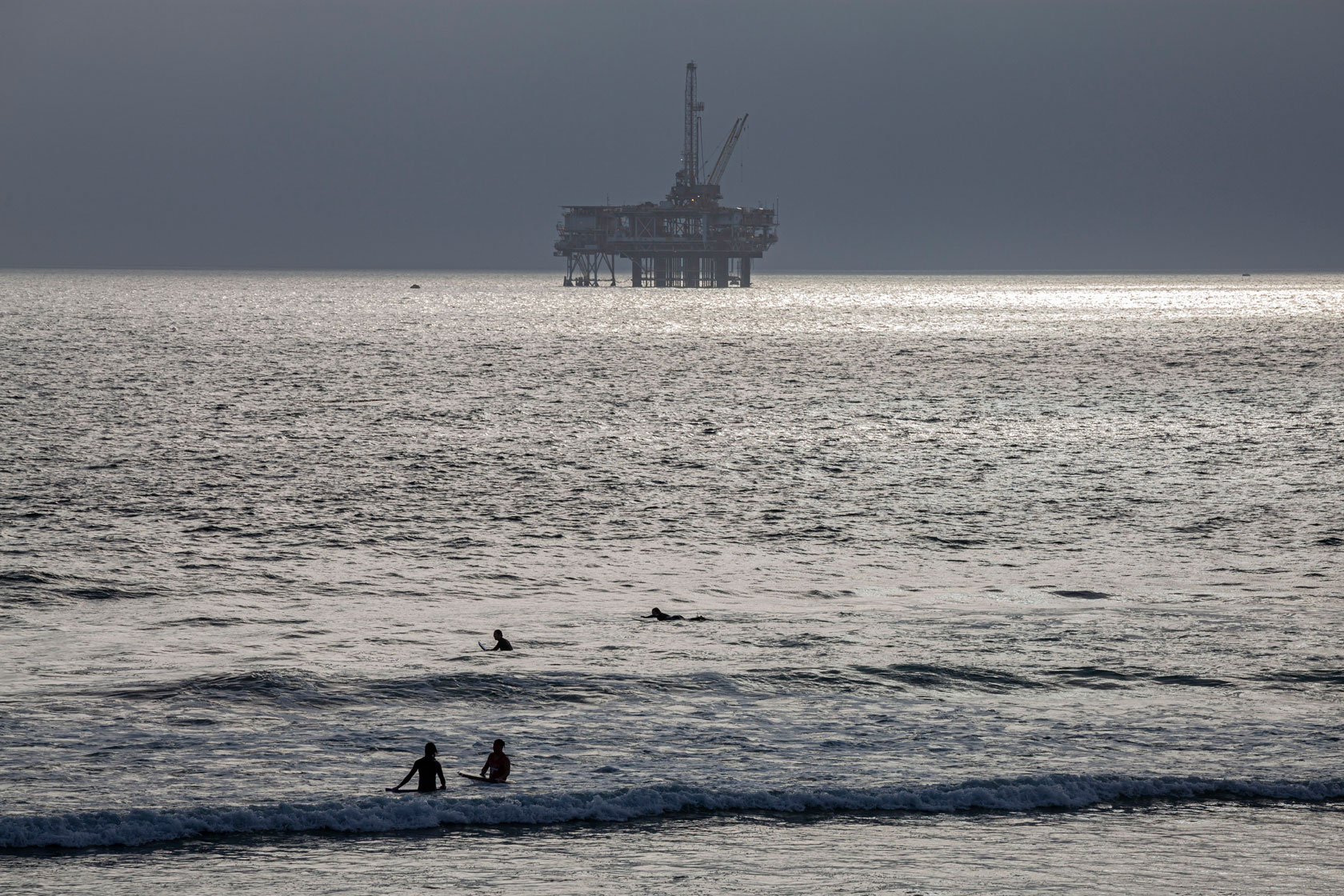 An oil Derrick and surfers off coast of Huntington Beach, Orange County, California.