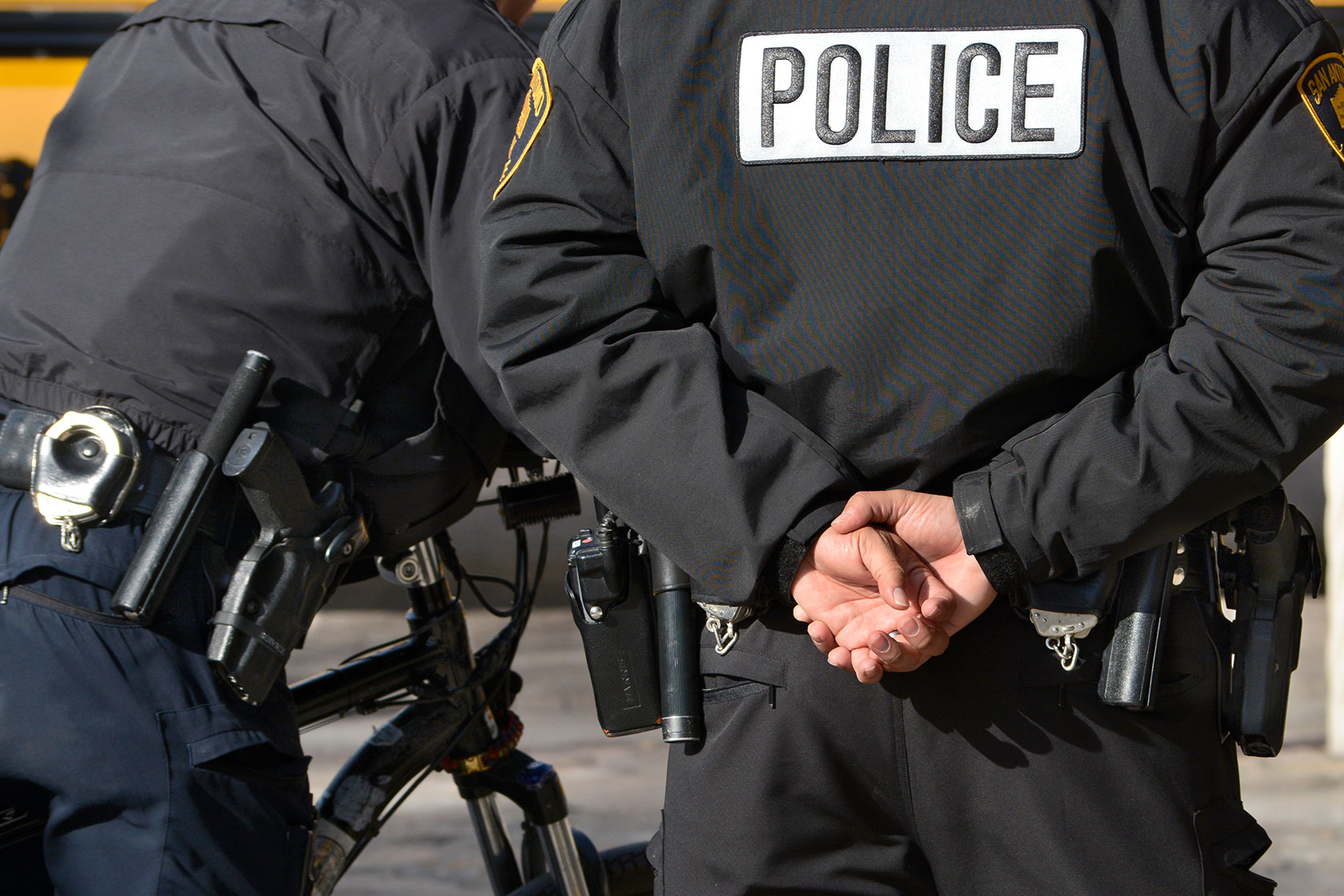 Photo shows two standing police officers from behind.