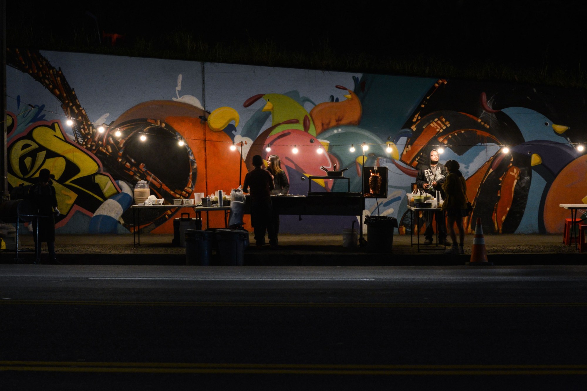 A California street vendor serves customers in front of a colorful mural in Los Angeles.