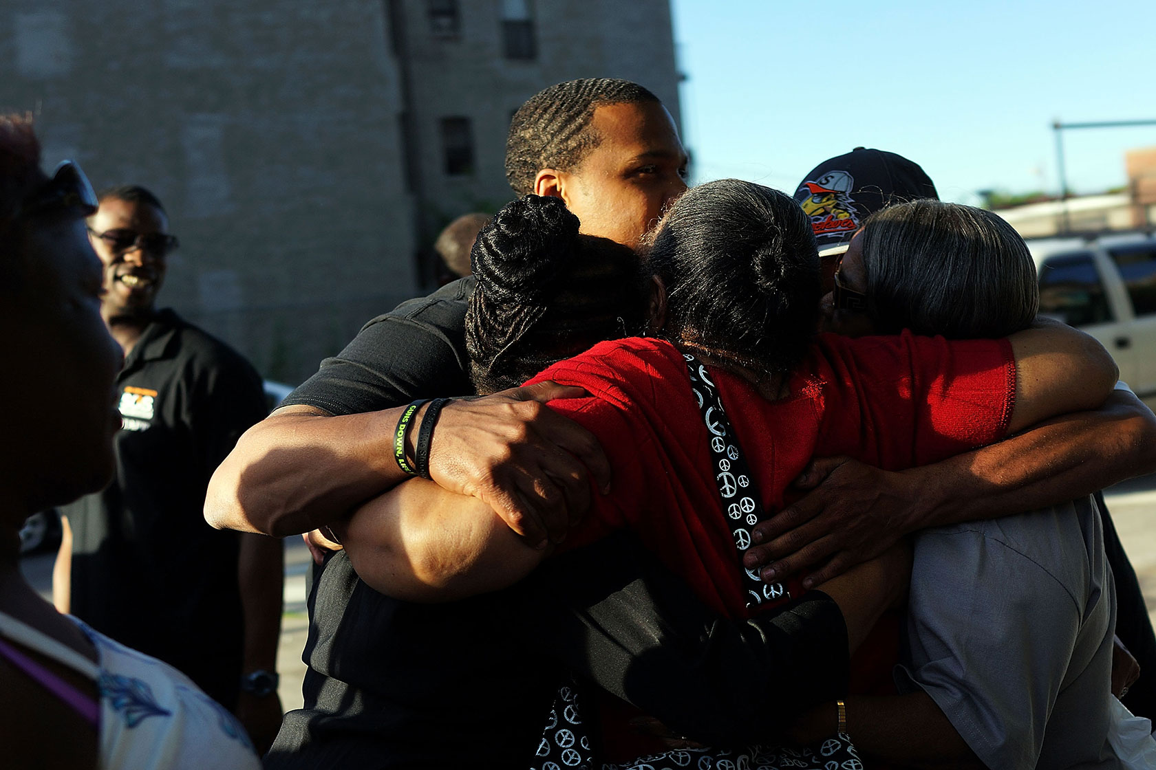 Photo shows a group of five people hugging.