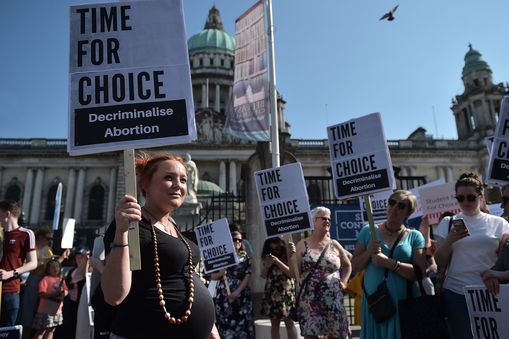 A pregnant woman and others protest against an anti-abortion referendum outside Belfast City Hall, holding signs that say 