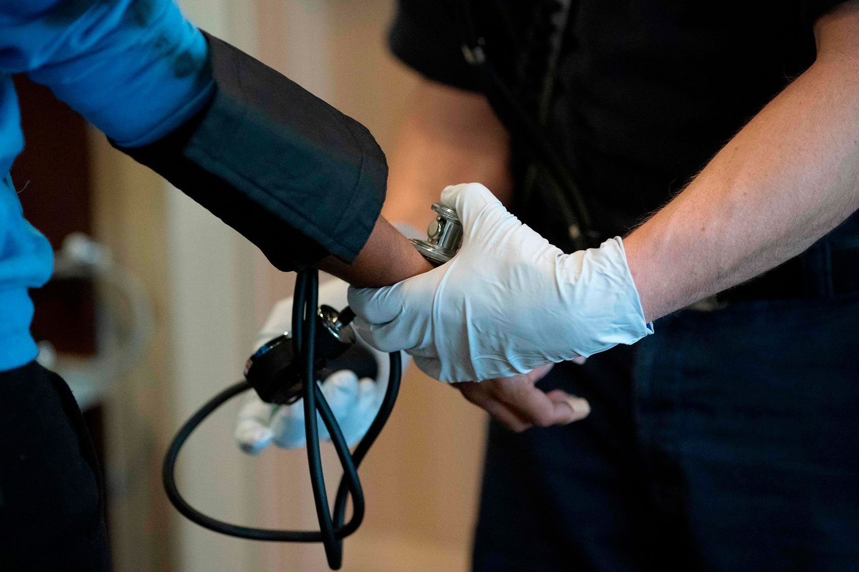 Photo shows a paramedic with gloved hands taking a person's blood pressure.