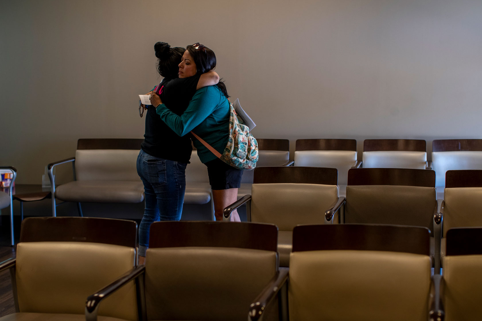 Photo shows two women hugging in a waiting room.