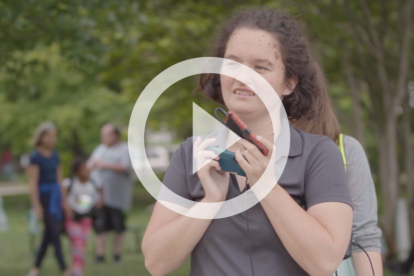 Emma, a nonspeaking autistic woman, smiles while holding her phone, which she uses to communicate.