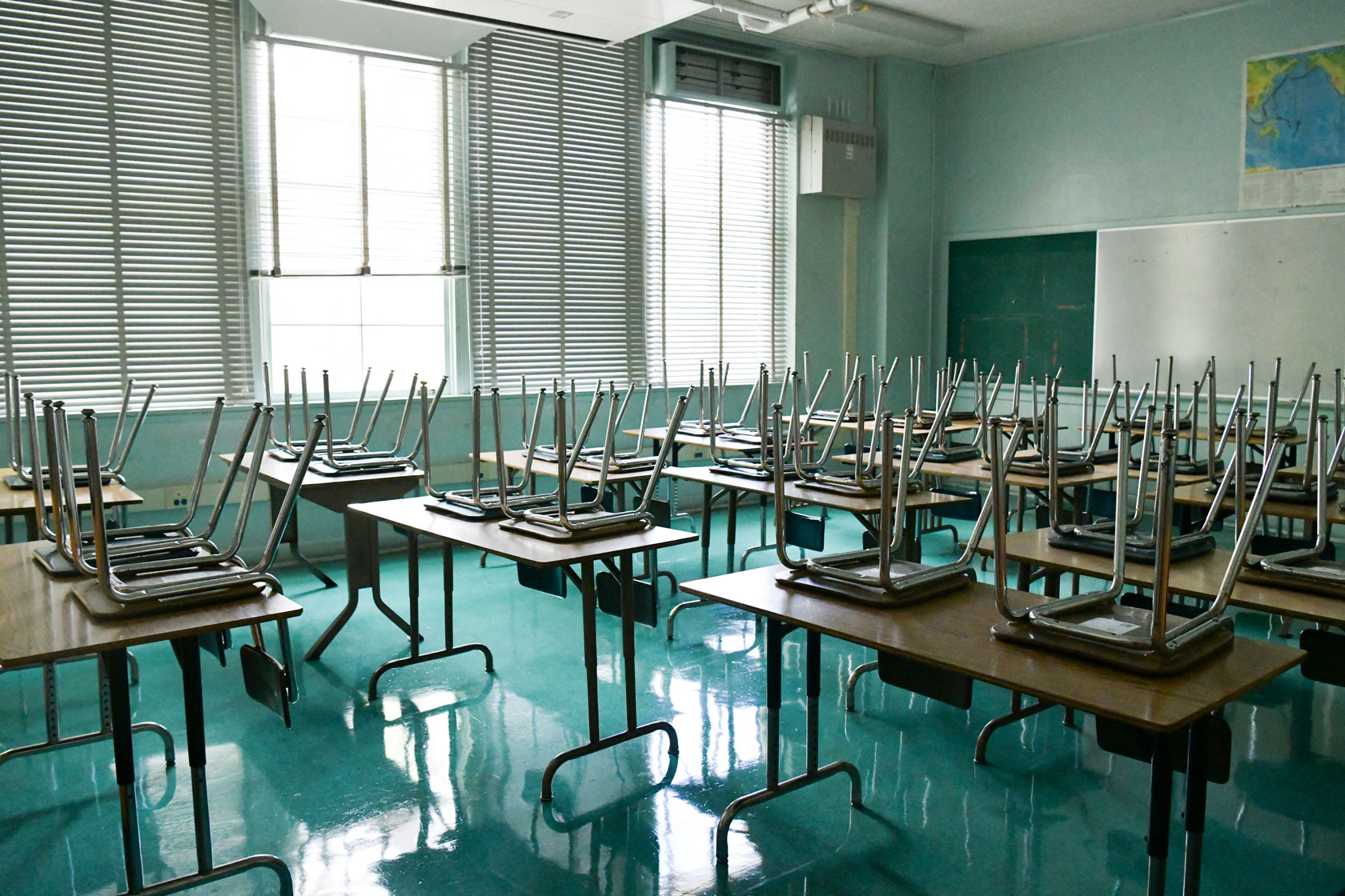Photo shows an empty classroom with chairs stacked on top of the desks.