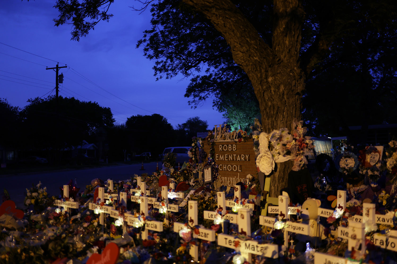 Photo shows wooden crosses displaying the victims' names in front of the Robb Elementary School sign.