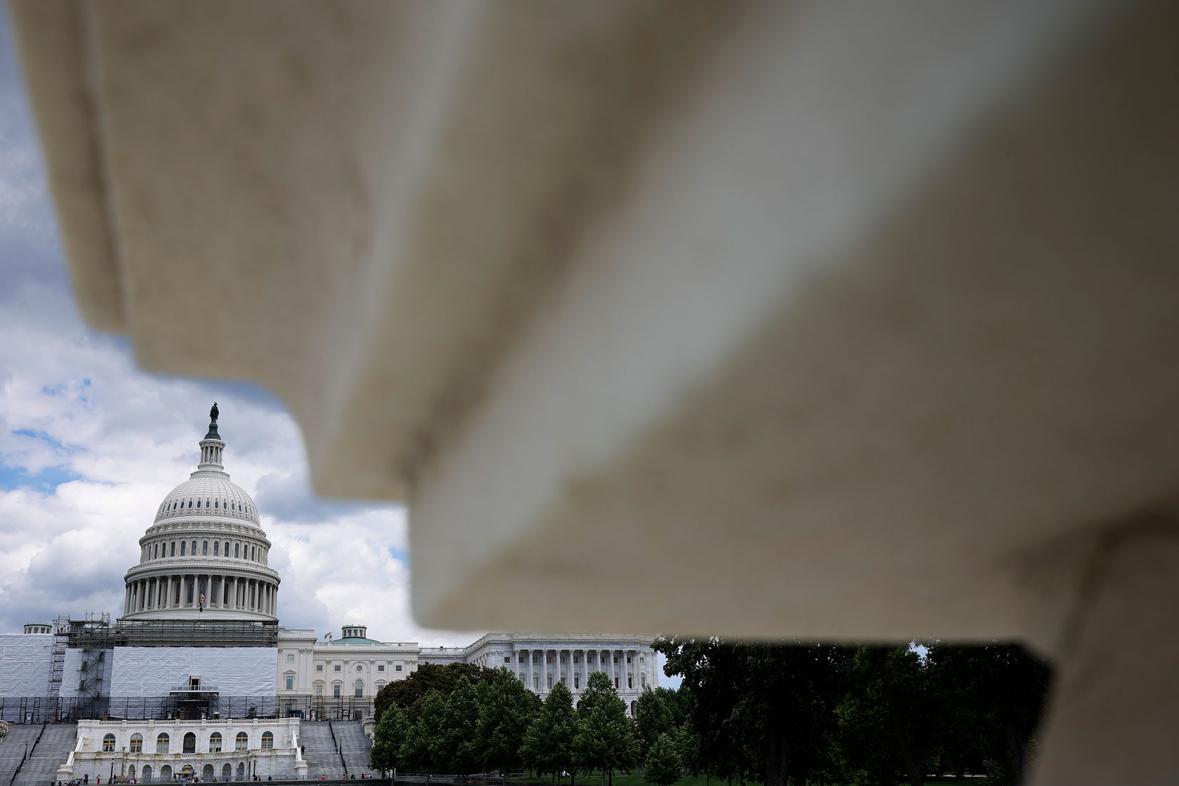 The Capitol undergoes construction in the background, with a white stone blurred in the foreground.