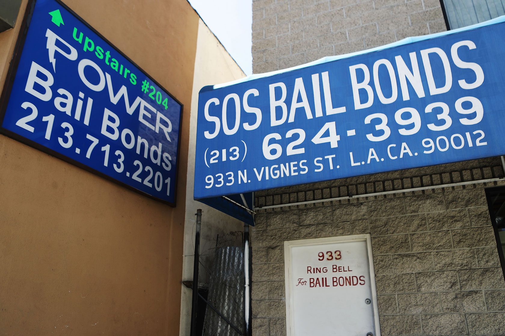Photo shows two blue signs on the side of a building advertising bail bonds, displaying the companies' phone numbers.