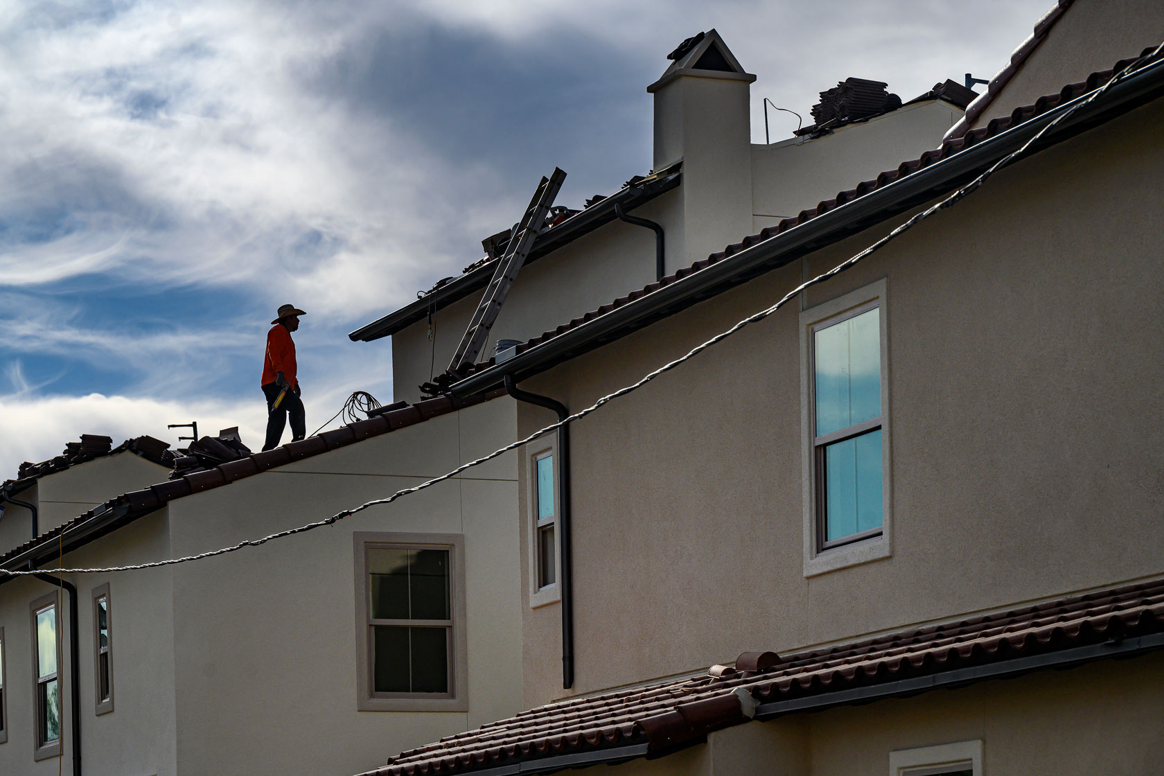 Photo shows a construction worker standing on the roof of a house.