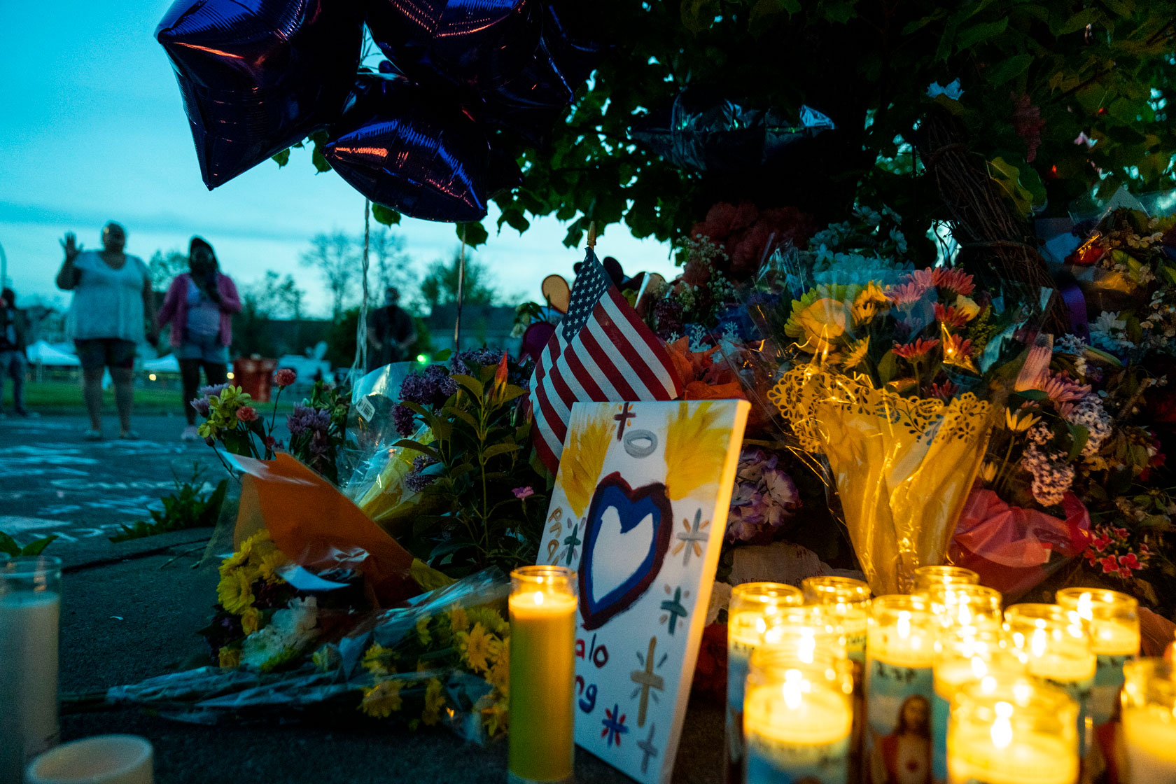 Mourners approach a memorial with flowers, candles, and balloons outside of a grocery store in Buffalo, New York, which was the scene of a mass shooting.