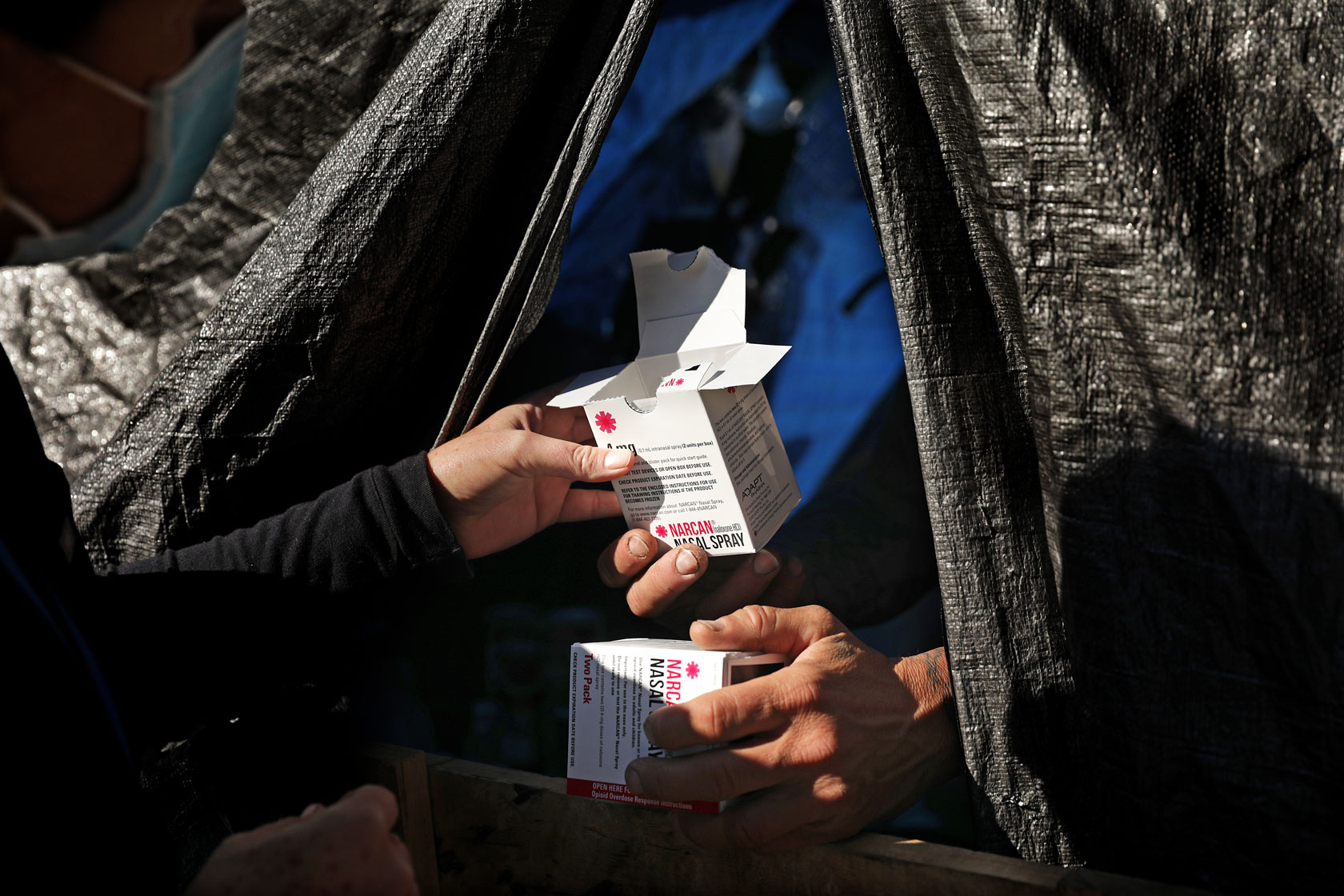 Photo shows a person handing a box of Narcan nasal spray to another person.