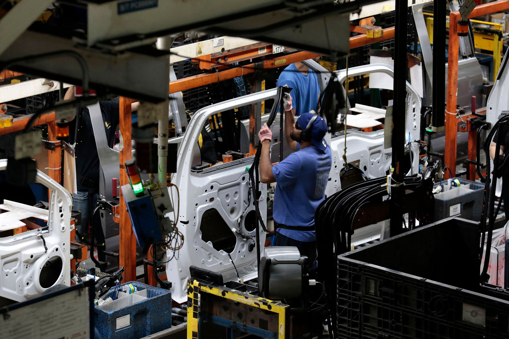 Photo shows a worker wearing blue working on a white car door at a factory.