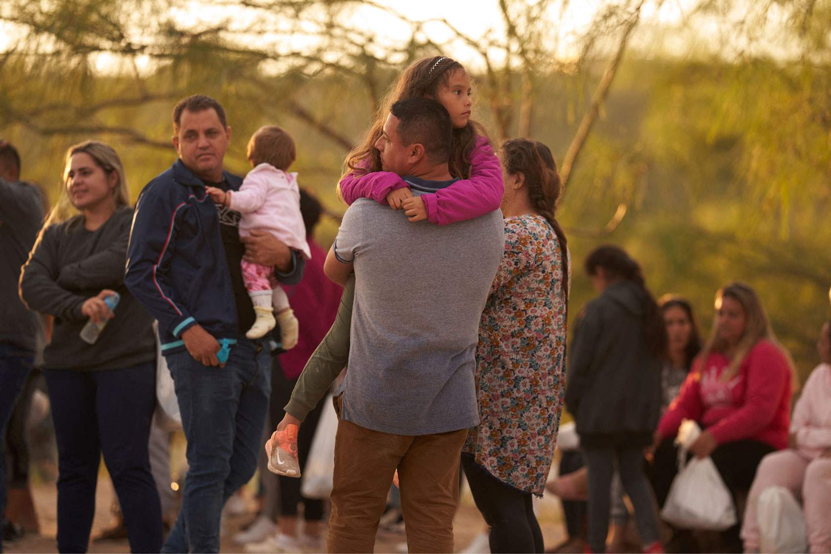 A group of migrants, with a father holding his young daughter in the foreground, stand near the U.S-Mexico border in Texas.