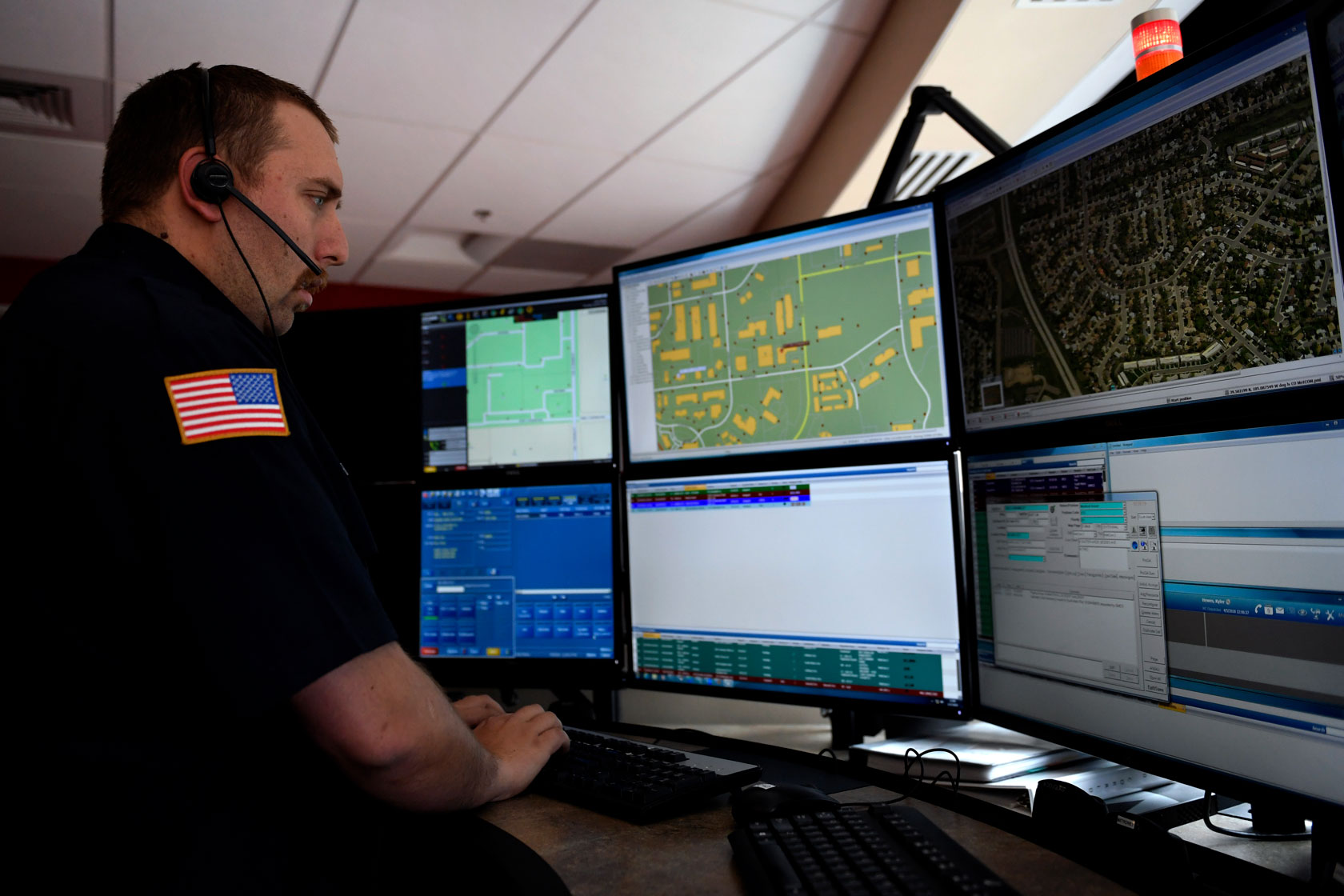 A dispatcher speaks to a caller while viewing various computer screens.