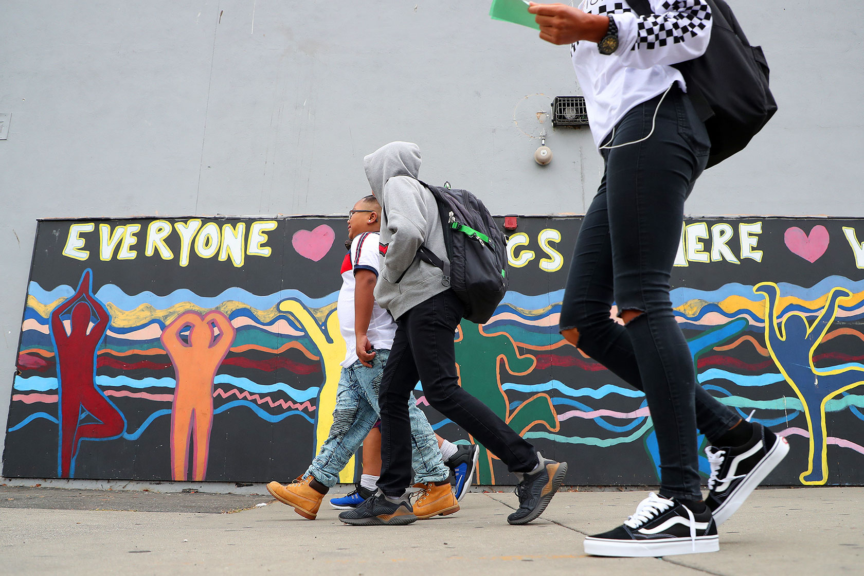 Photo shows several students walking in front of a colorful mural.