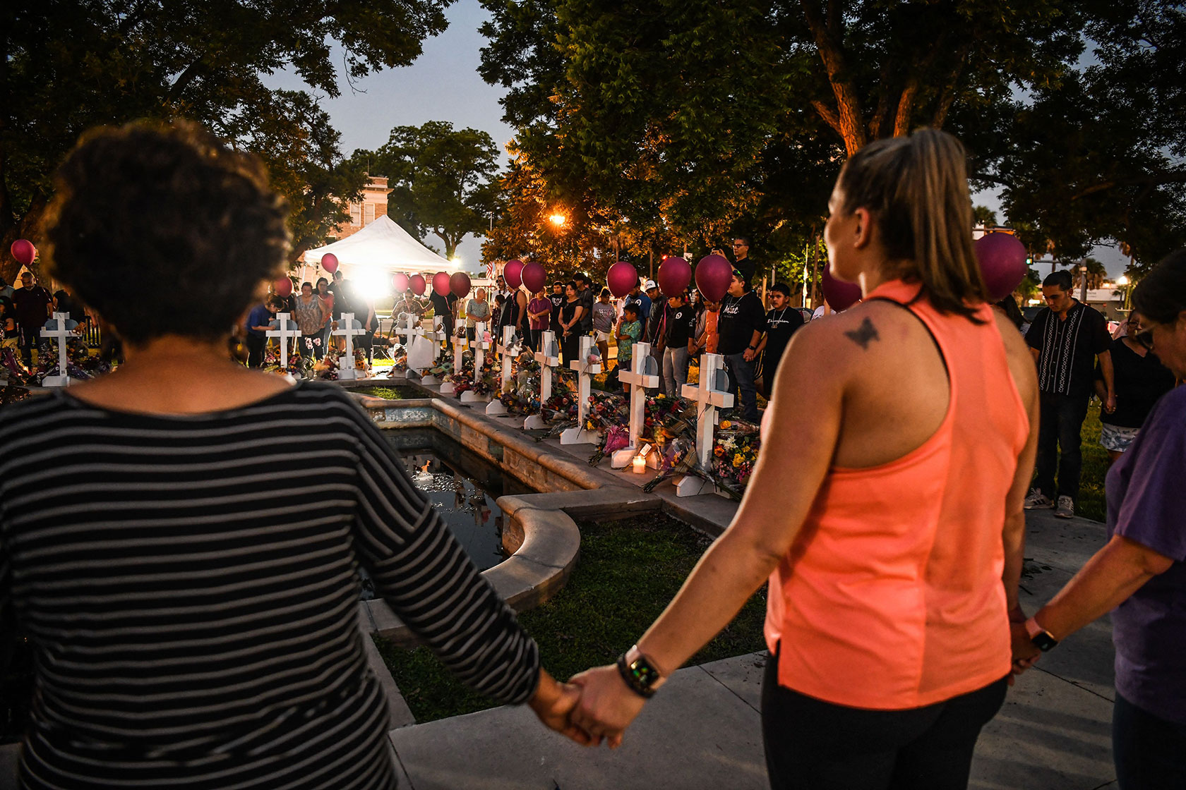 Photo shows a group of people standing in a circle and holding hands around a makeshift memorial.