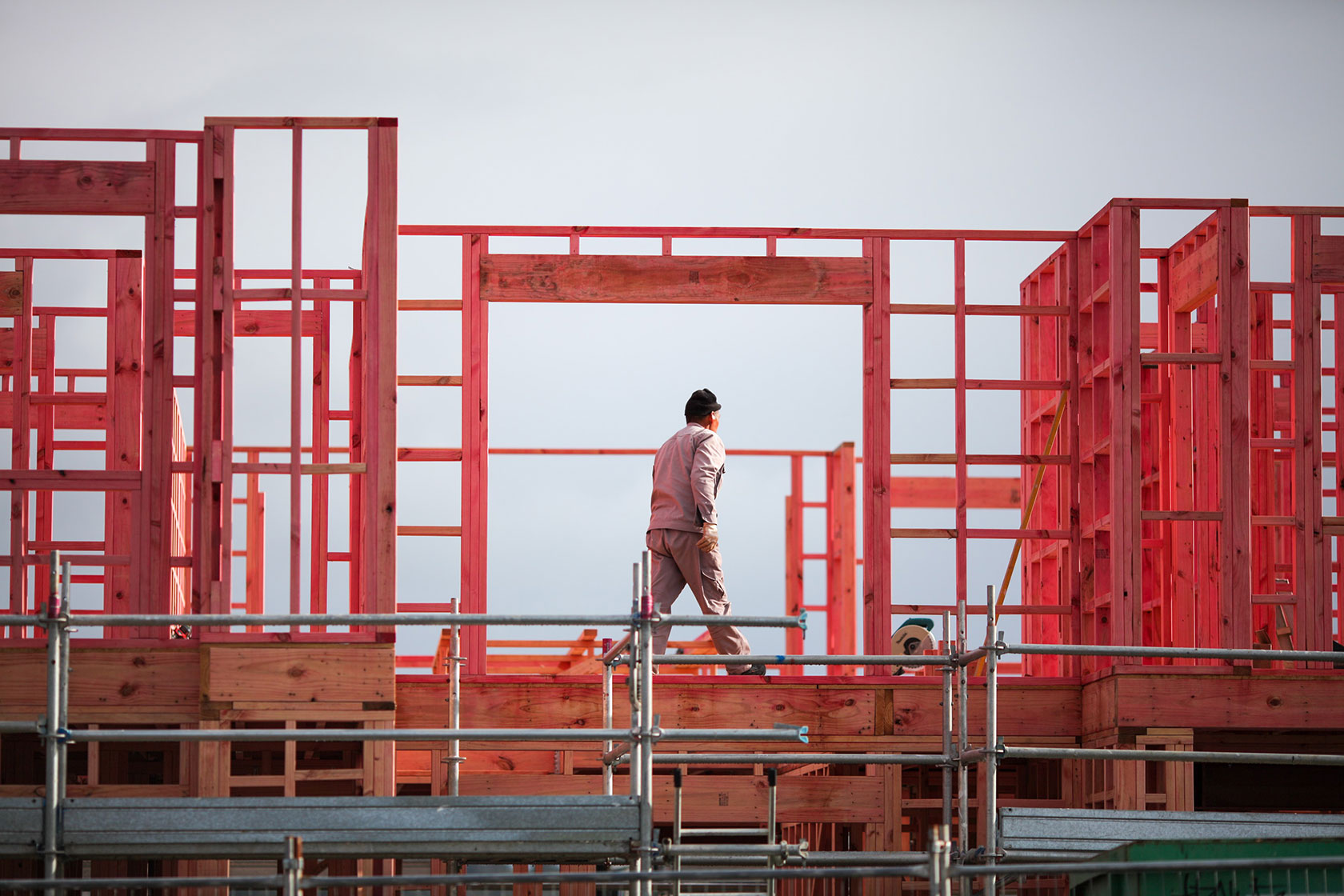 Photo shows a man walking across a partially constructed wooden structure.
