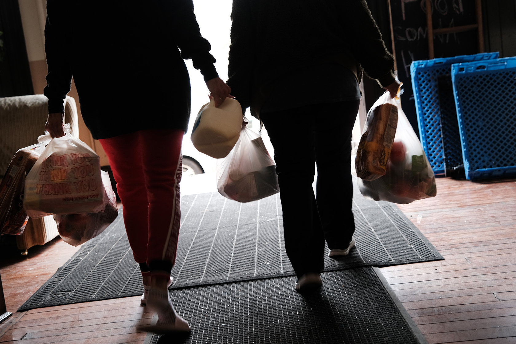 Two people, faces not shown, carrying grocery bags of food