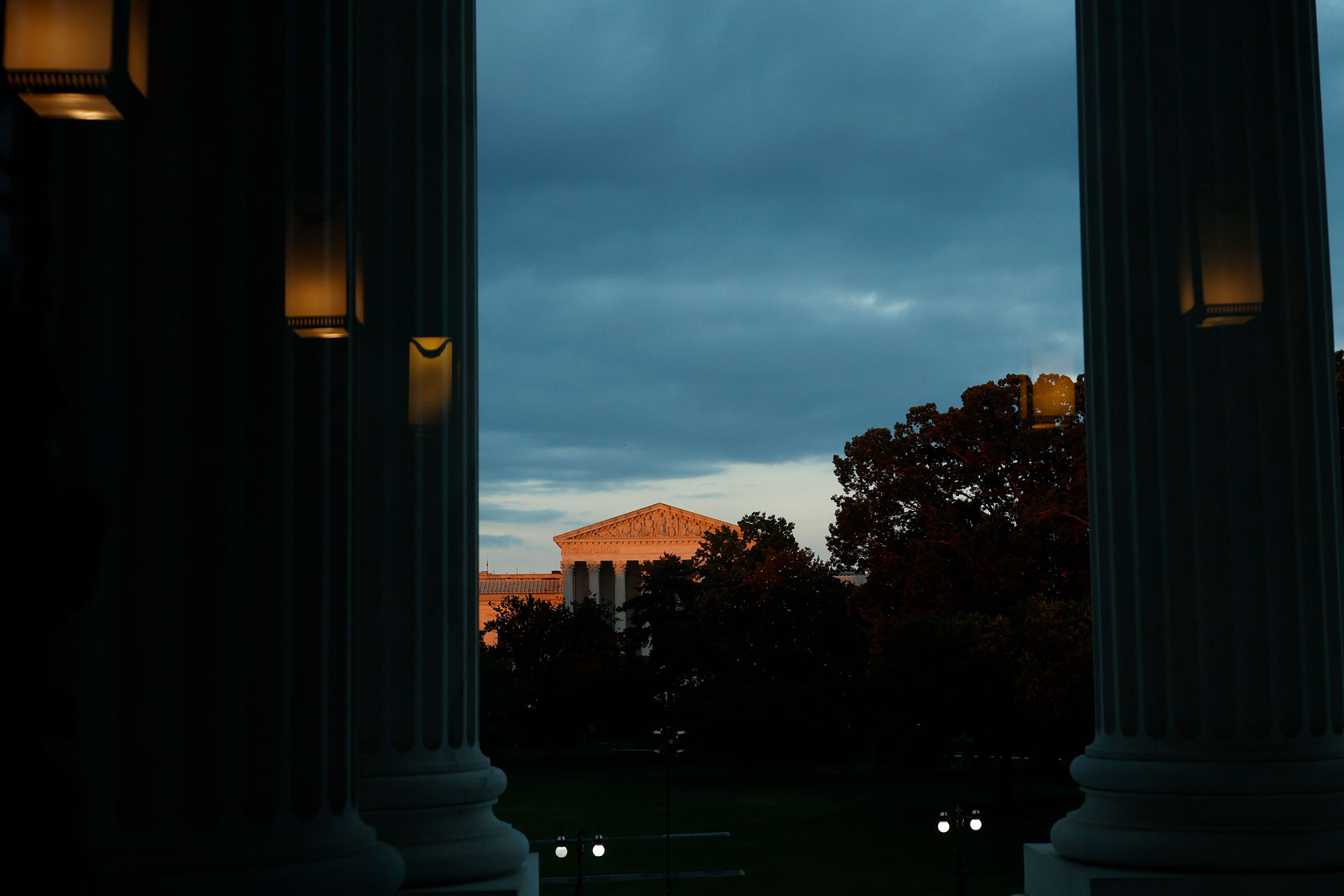 Photo shows a partial view of the Supreme Court building illuminated by late-afternoon light, with trees partly obstructing the view.