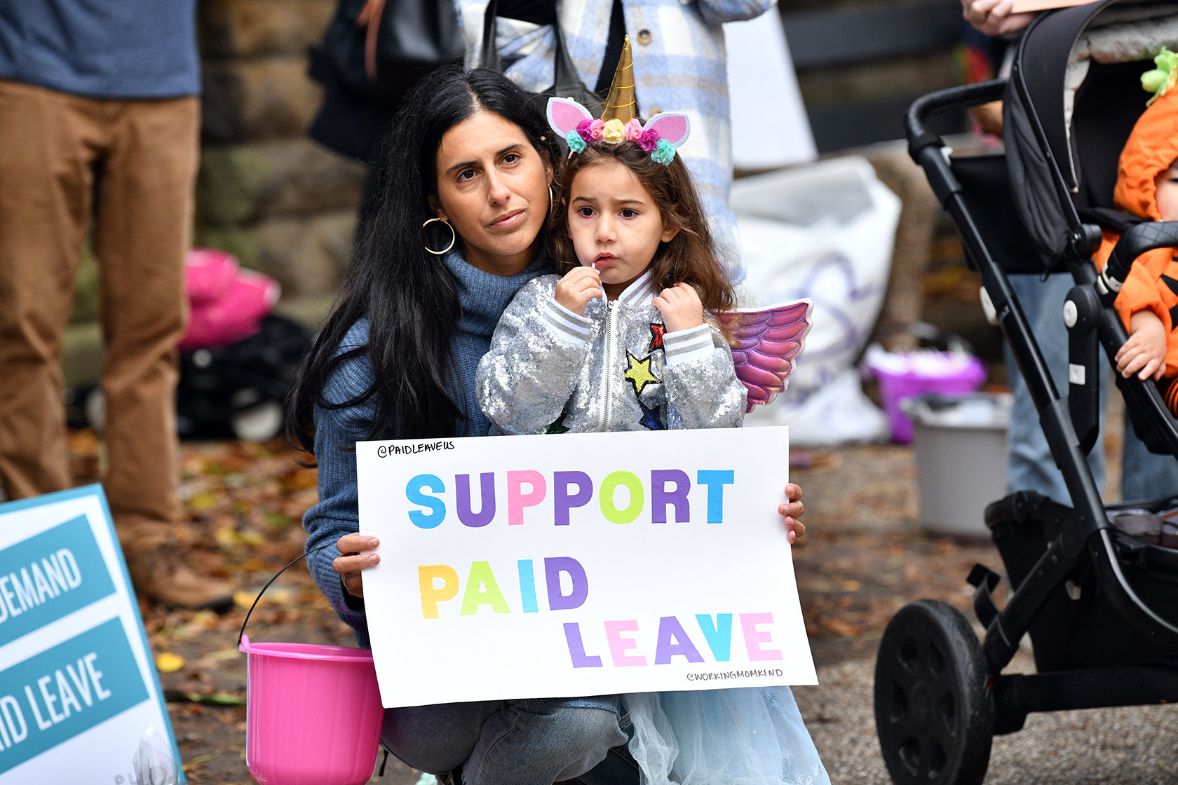 Person, with child, holding sign that says Support for Paid Leave