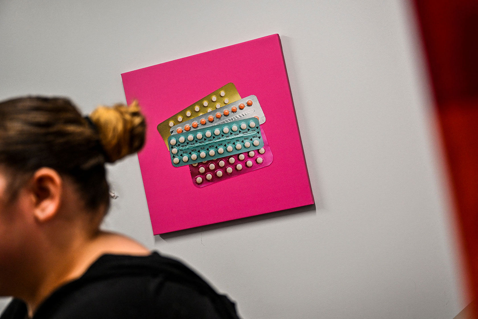 Artwork depicting contraceptive pills is seen behind a woman waiting at a family planning center.